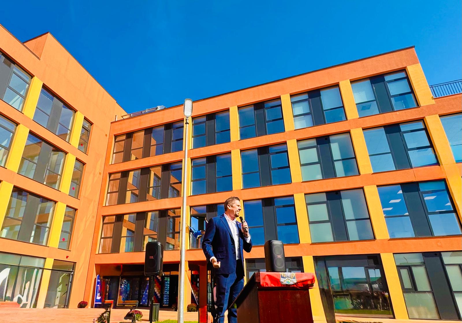 Dr. Wilkens speaking at a podium in front of the modern campus building